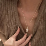 Close-up of a model elegantly displaying the massive 10 carat oval rose gold solitaire necklace, hand resting on her chest.