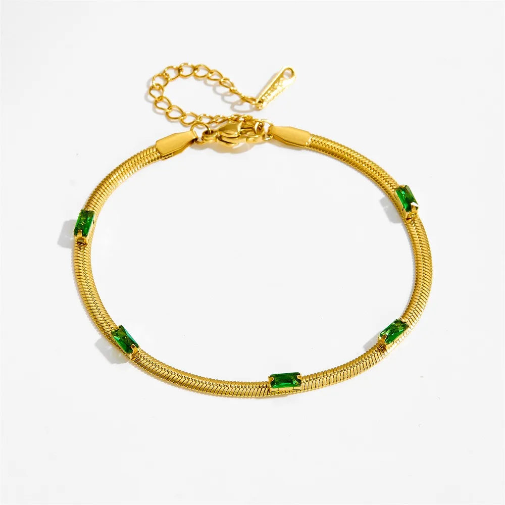 Angled view of a 14K gold plated snake chain bracelet featuring five green baguette-cut cubic zirconia stones, a lobster clasp, and an extender chain, isolated on a clean white background.
