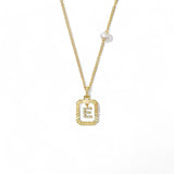 A 14K gold plated vintage rectangular sunburst pendant featuring a dancing pave initial letter E and a side freshwater pearl, isolated on a white background.