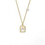 A 14K gold plated vintage rectangular sunburst pendant featuring a dancing pave initial letter H and a side freshwater pearl, isolated on a white background.