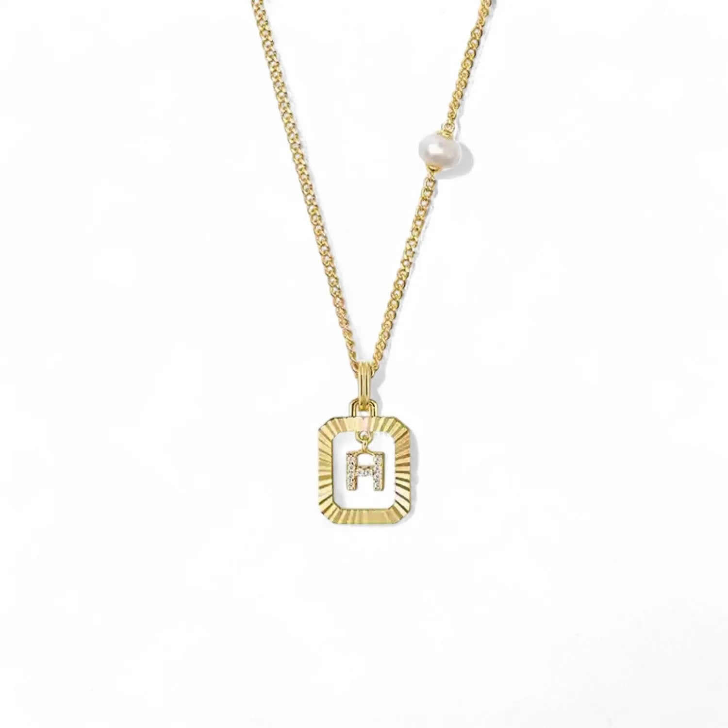 A 14K gold plated vintage rectangular sunburst pendant featuring a dancing pave initial letter H and a side freshwater pearl, isolated on a white background.
