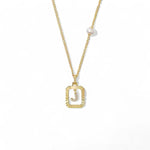A 14K gold plated vintage rectangular sunburst pendant featuring a dancing pave initial letter J and a side freshwater pearl, isolated on a white background.