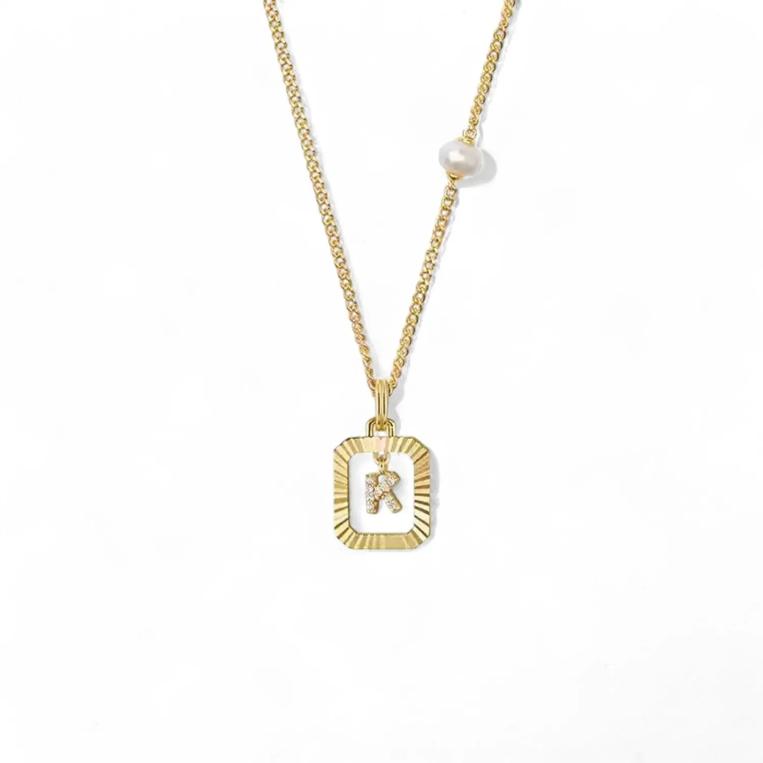 A 14K gold plated vintage rectangular sunburst pendant featuring a dancing pave initial letter K and a side freshwater pearl, isolated on a white background.