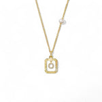 A 14K gold plated vintage rectangular sunburst pendant featuring a dancing pave initial letter O and a side freshwater pearl, isolated on a white background.