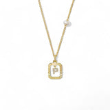 A 14K gold plated vintage rectangular sunburst pendant featuring a dancing pave initial letter P and a side freshwater pearl, isolated on a white background.