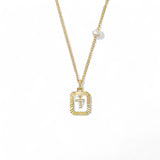 A 14K gold plated vintage rectangular sunburst pendant featuring a dancing pave initial letter T and a side freshwater pearl, isolated on a white background.