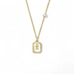 A 14K gold plated vintage rectangular sunburst pendant featuring a dancing pave initial letter X and a side freshwater pearl, isolated on a white background.