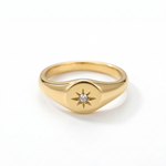 A dainty solid gold signet ring featuring an engraved starburst motif with a small round natural diamond set in the center, isolated on a white background.
