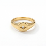 A dainty solid gold signet ring featuring an engraved starburst motif with a small round natural diamond set in the center, isolated on a white background.