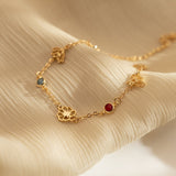 A delicate 18K gold-plated bracelet featuring custom cutout birth flowers and bezel-set birthstones resting beautifully on beige silk.
