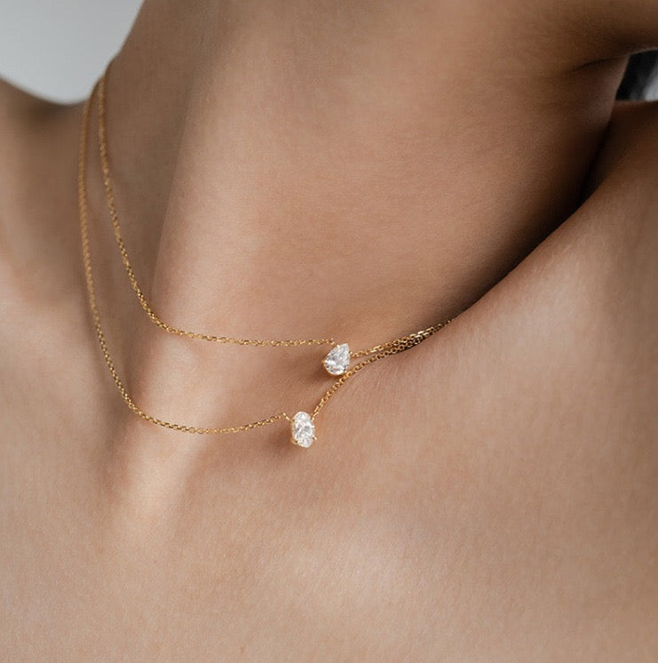 Front view of a model wearing an adjustable 18k gold layered necklace set, highlighting the perfect spacing between the oval and teardrop pendants.