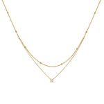 A delicate 18K gold plated double layered necklace featuring a top beaded satellite chain and a bottom chain with a single 4mm round clear CZ pendant, isolated on a clean white background.