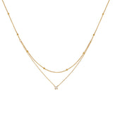 A delicate 18K gold plated double layered necklace featuring a top beaded satellite chain and a bottom chain with a single 4mm round clear CZ pendant, isolated on a clean white background.