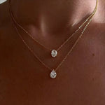 Close-up of a woman wearing an 18k gold plated layered necklace set featuring diamond-like oval and teardrop solitaire pendants.