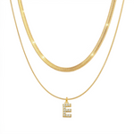 Two 18K gold plated necklaces layered together, featuring a flat snake chain and a matching chain with a pave initial E pendant, isolated on a clean white background.