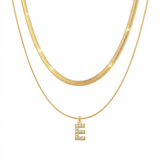 Two 18K gold plated necklaces layered together, featuring a flat snake chain and a matching chain with a pave initial E pendant, isolated on a clean white background.