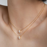 Side profile of a woman's collarbone showcasing two dainty 18k gold chain necklaces with brilliant-cut oval and pear gemstones.