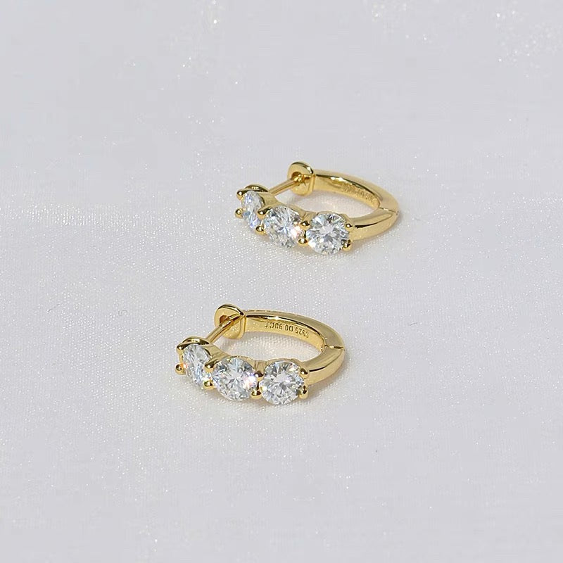 A pair of 18K gold-plated huggie hoop earrings featuring three sparkling stones and a secure click-in clasp on a white background.