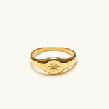 Front view of a dainty gold-plated signet ring with a deeply engraved eight-point starburst motif and no center stone, on a white background.