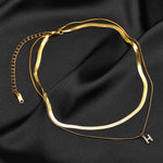 Two layered 18K gold plated necklaces, one flat snake chain and one with a pave initial H pendant, displayed together on black satin fabric, showing the adjustable extender chain and clasp.