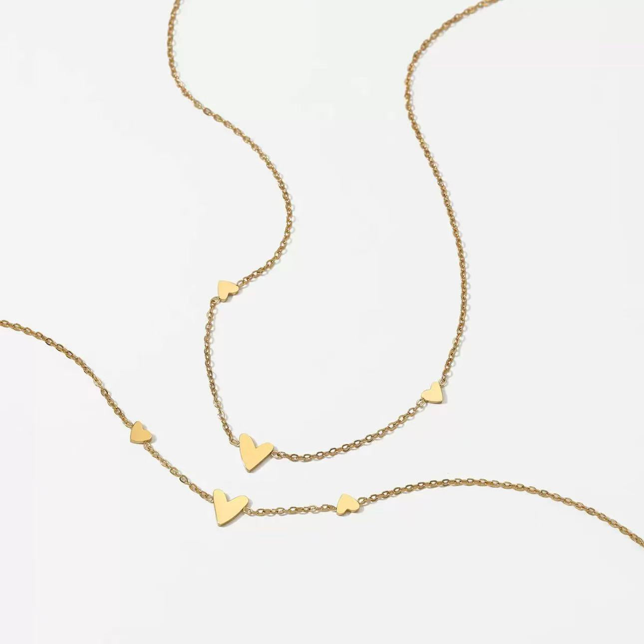 Flat lay of the 18K gold plated necklace with tiny heart charms resting elegantly on a textured beige surface.