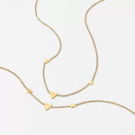 Flat lay of the 18K gold plated necklace with tiny heart charms resting elegantly on a textured beige surface.