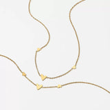 Flat lay of the 18K gold plated necklace with tiny heart charms resting elegantly on a textured beige surface.