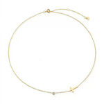 Flat lay of the 18K gold sideways cross necklace displayed on a textured stone background.