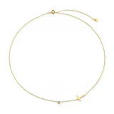 Flat lay of the 18K gold sideways cross necklace displayed on a textured stone background.