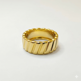 A chunky 18K gold band ring featuring a diagonal ribbed texture and a smooth interior, displayed against a seamless white background.