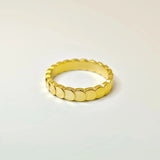 Flat lay product shot of an 18k gold scalloped circle band resting on a white surface, highlighting its reflective finish.