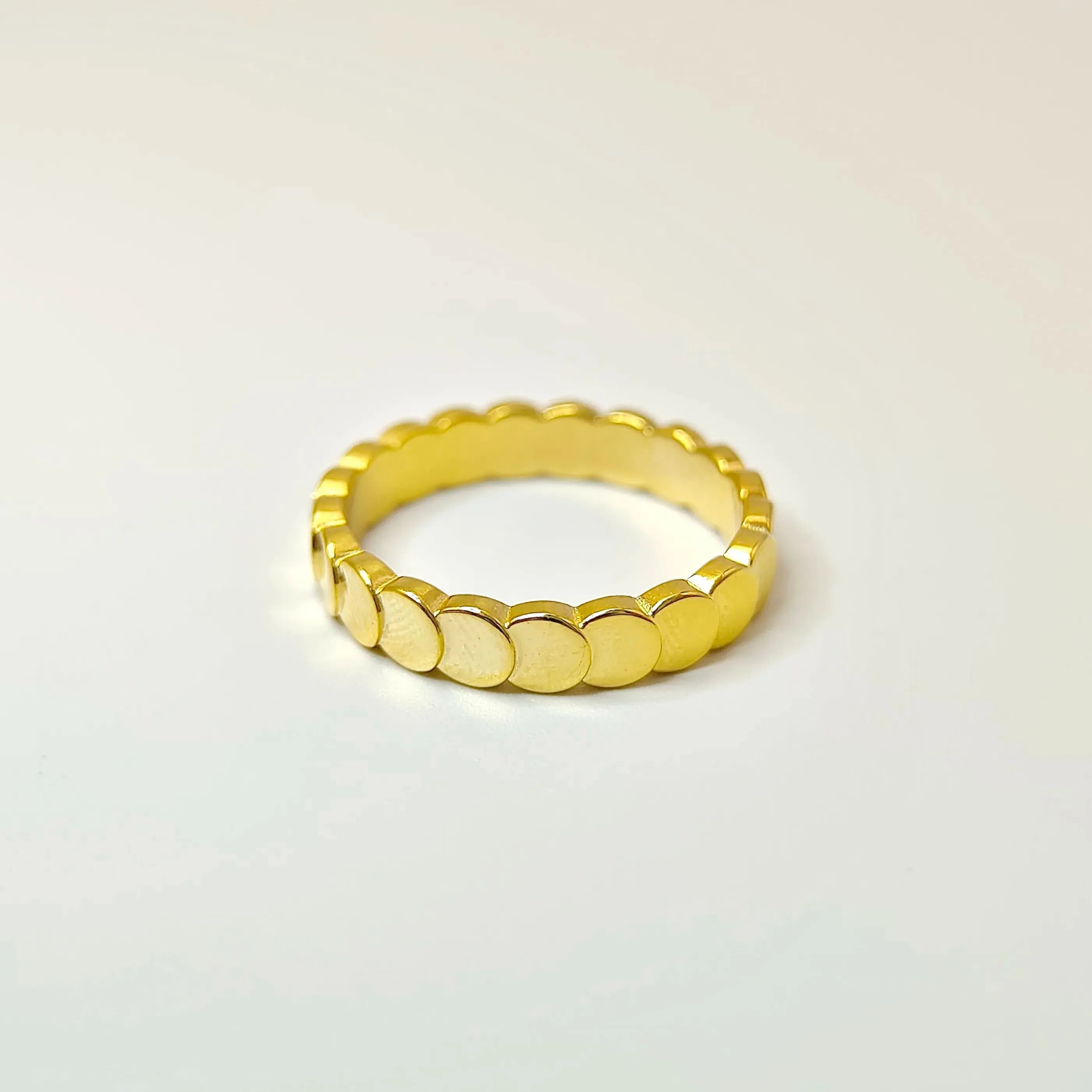 Flat lay product shot of an 18k gold scalloped circle band resting on a white surface, highlighting its reflective finish.