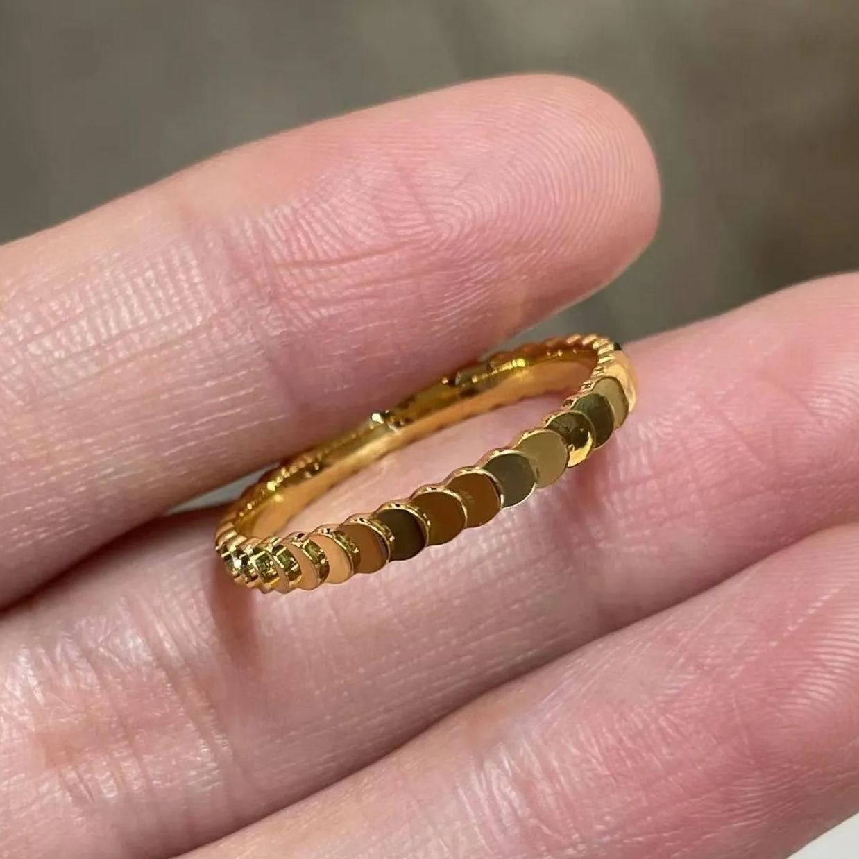 Macro close-up of an 18k gold disc ring held between two fingers, emphasizing the smooth, polished overlapping coin design.