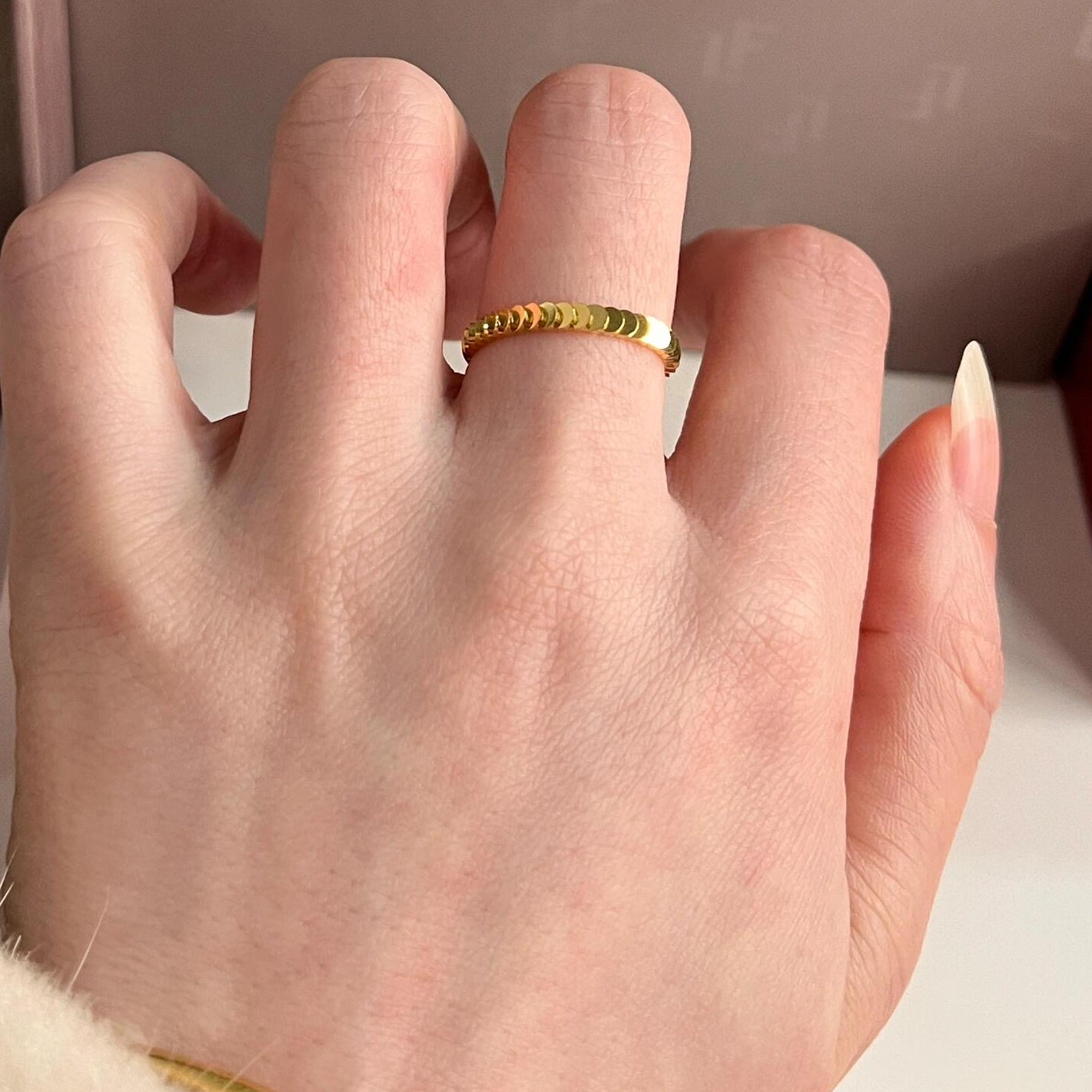 Close-up of an 18k gold stackable coin ring worn on a woman's index finger, highlighting the scalloped edges.