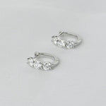 A pair of premium 925 sterling silver huggie hoop earrings featuring three brilliant-cut stones, isolated on a white background.