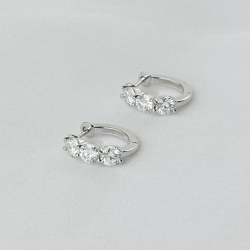 A pair of premium 925 sterling silver huggie hoop earrings featuring three brilliant-cut stones, isolated on a white background.