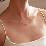Gold necklace with heart pendants on a person wearing a white top.