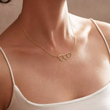 Gold necklace with heart pendants on a person wearing a white top.
