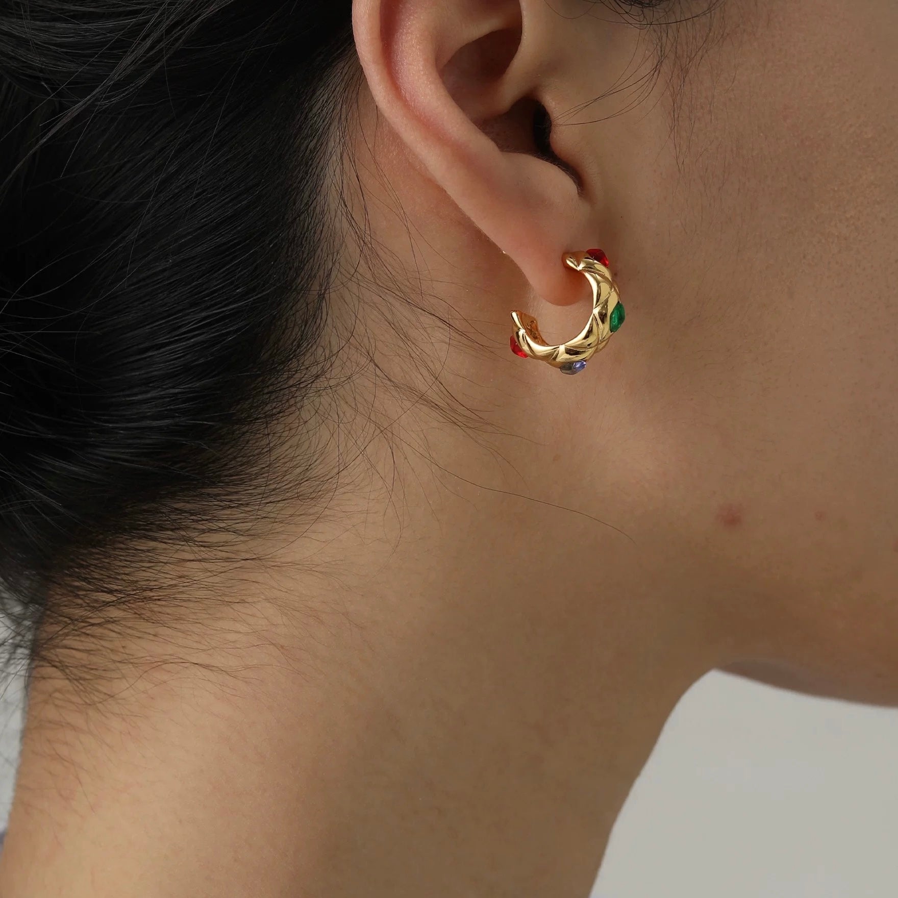 Gold earring with colorful stones worn by a person