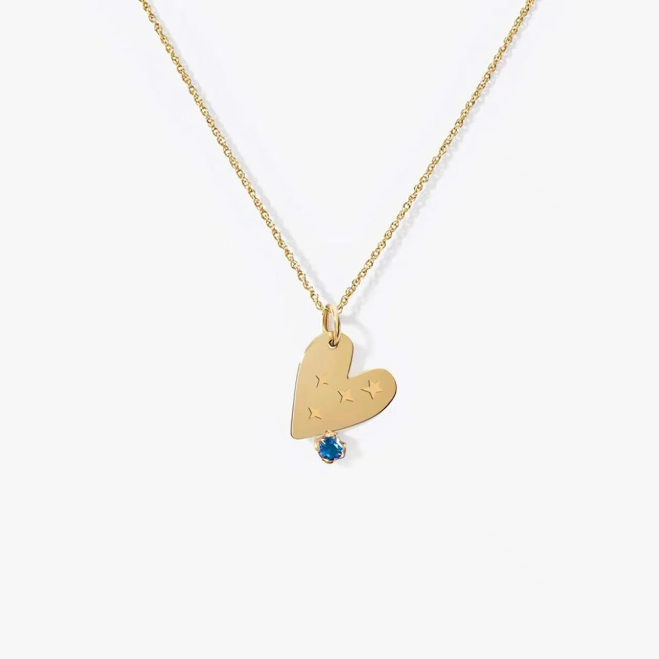 Close-up of personalized gold heart necklace with star engravings and blue gemstone on white background