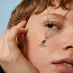 Close-up of a person wearing a gold necklace with a pendant against a light blue background