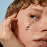 Close-up of a person wearing a gold necklace with a pendant against a light blue background