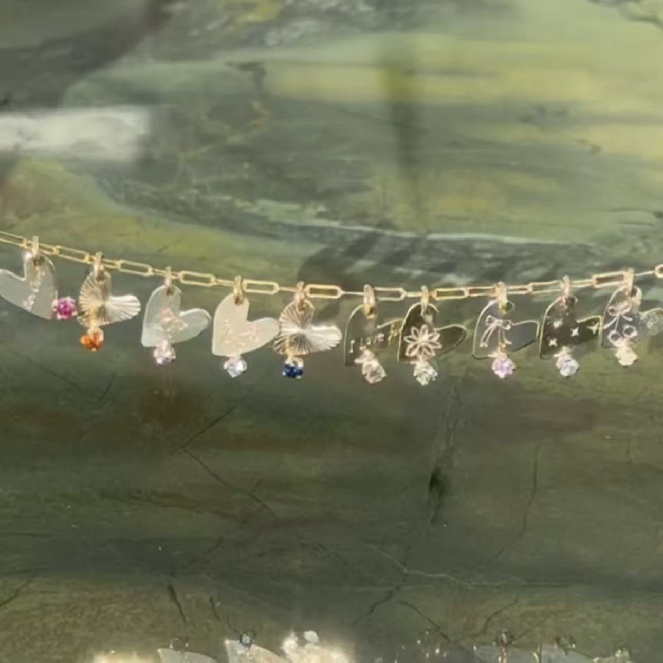 Gold chain with heart-shaped pendants on a reflective surface