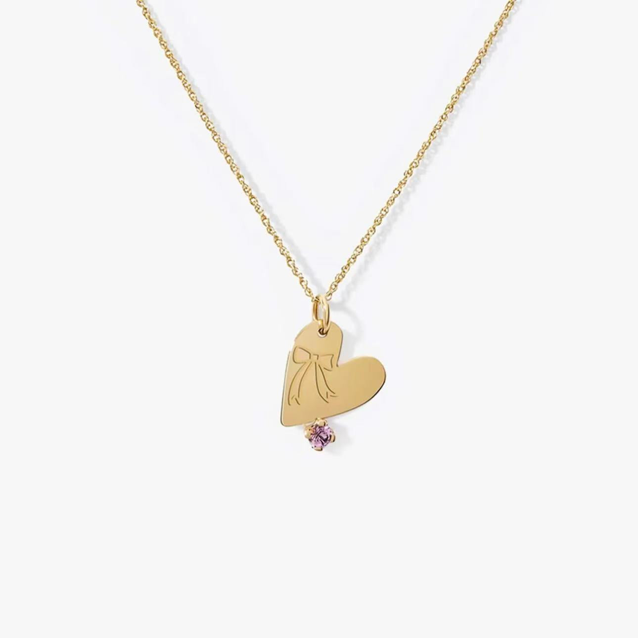 Close-up of personalized gold heart necklace with bowknot engraving and purple gemstone on white background