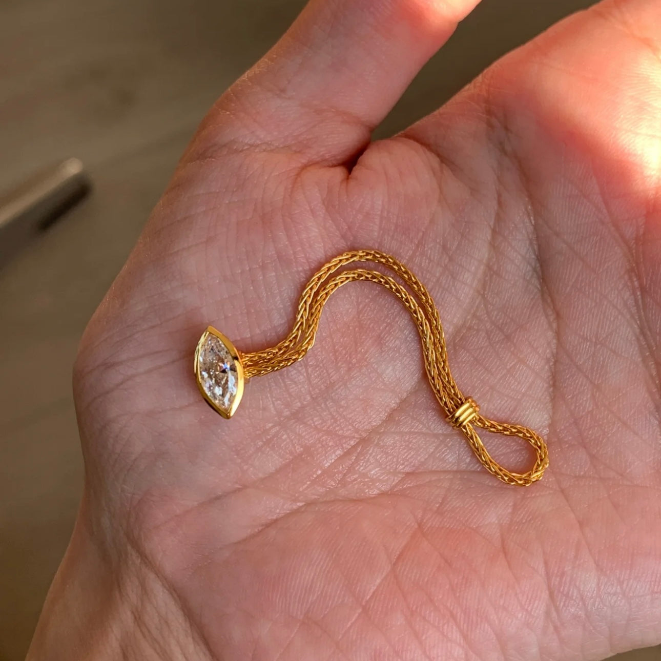 Gold ring with a marquise-shaped pendant held in a hand.