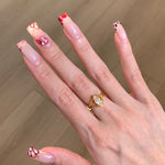 Hand with stylish nail art and a gold ring on a wooden surface