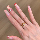 Hand with stylish nail art and a gold ring on a wooden surface