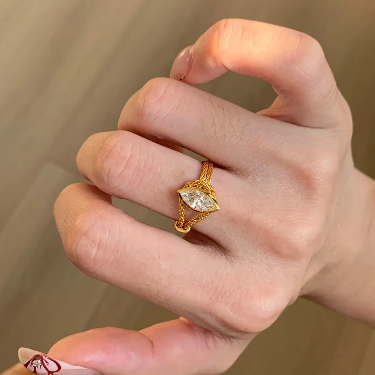 Hand wearing a gold ring with a diamond on a neutral background