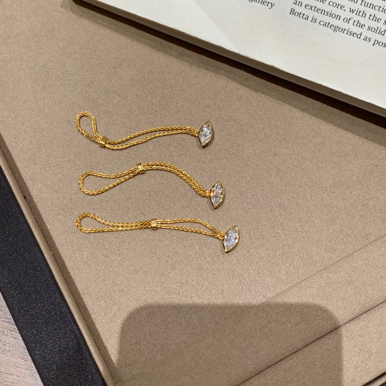 Gold rings with marquise-shaped pendants on a textured surface