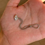 Silver ring with a teardrop-shaped pendant held in a hand.